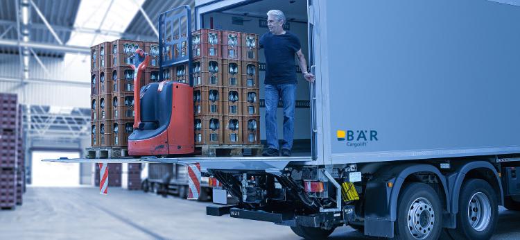 Vrachtwagenchauffeur lost drankbestelling en een elektrische palletwagen met een BAR laadklep in een hal