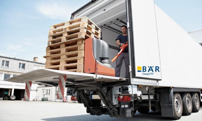Open, onderrijdbare BAR-laadbrug, waarop een persoon een lege pallet in het voertuig schuift