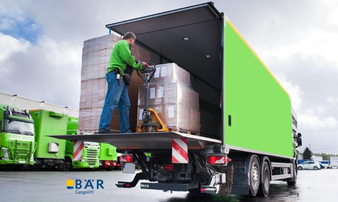 Vrachtwagenchauffeur schuift pallets met een palletwagen van het BAR-liftplatform in de vrachtwagen