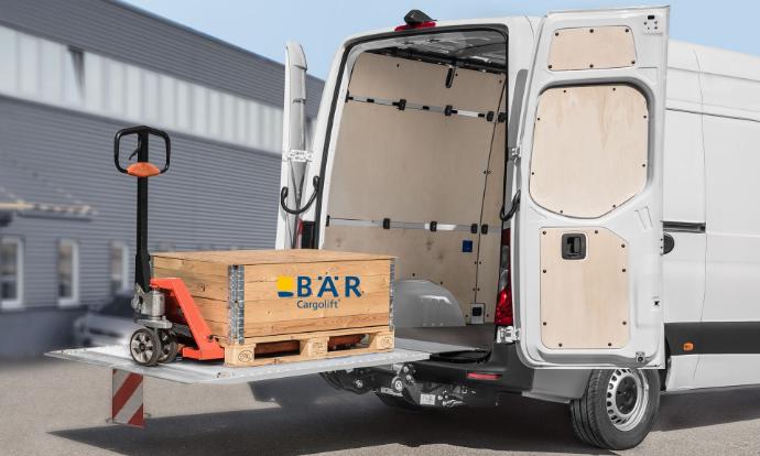 Op het uitgeklapt, opgeheven platform van de Bar VanLift staat een pallet met een palletwagen