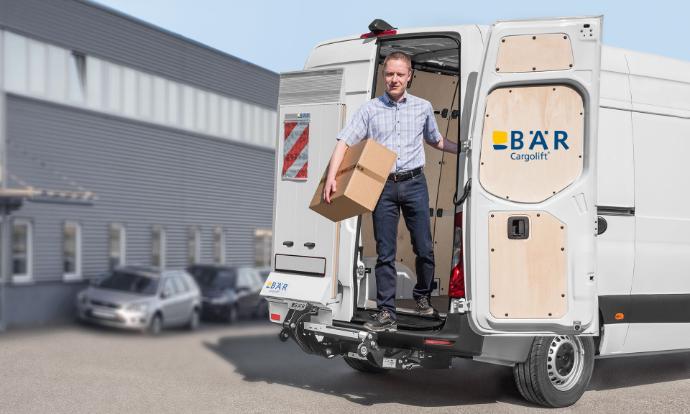 Man stapt met pakket uit bestelwagen via achterdeur, terwijl de Bär VanLift FreeAccess onbeweeglijk blijft