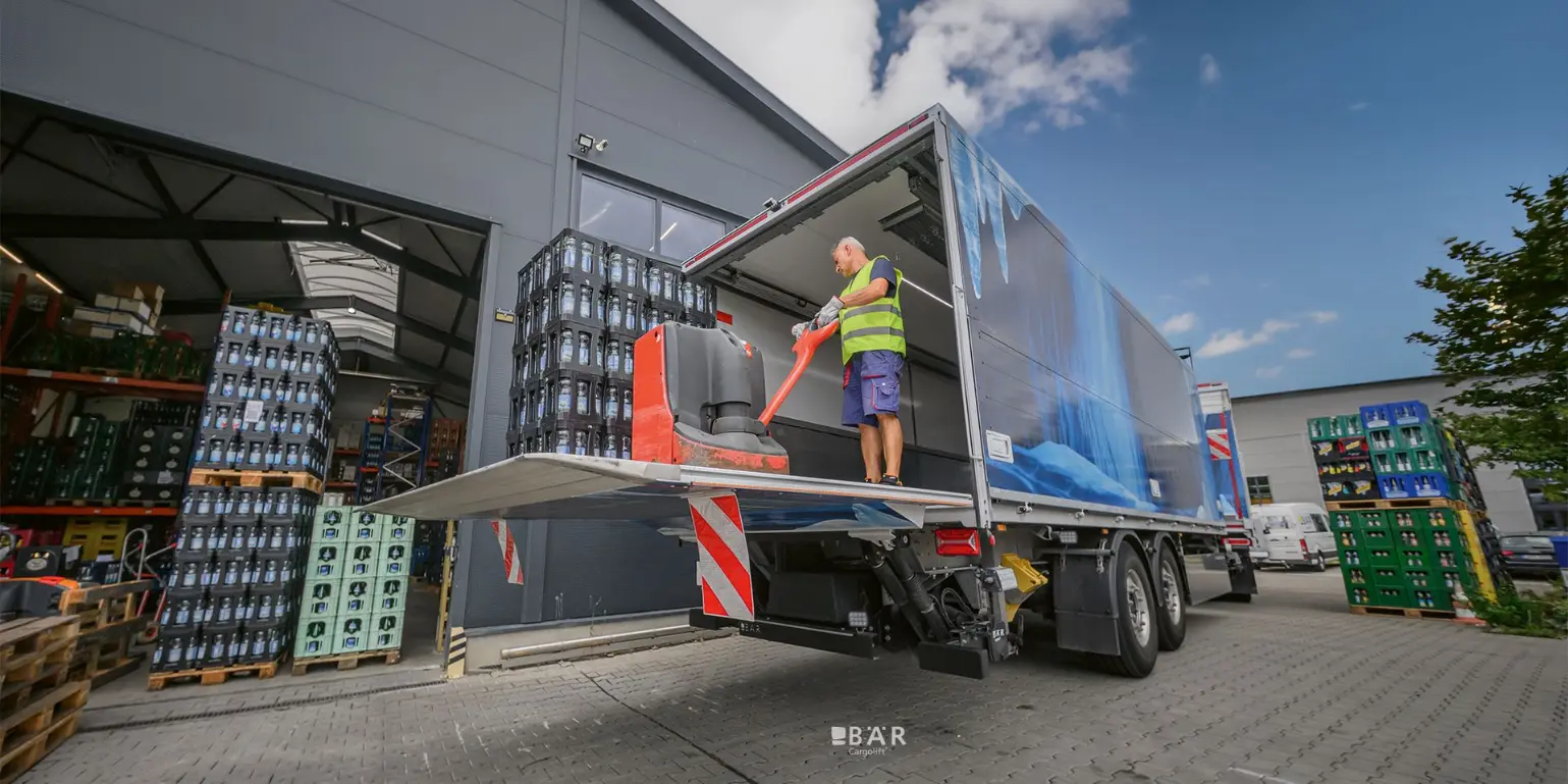 Man lost een drankpallet met een palletwagen via een Bar Cargolift gemonteerd op de aanhanger van een combinatie